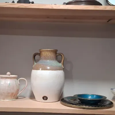 Assorted studio pottery and ceramics displayed on a wooden shelf, including a pink marbled vase, a light pink teapot, a large...