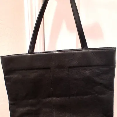 Vintage black leather tote bag featuring a stitched geometric design on the front and dual shoulder straps, shown hanging from a doorknob.