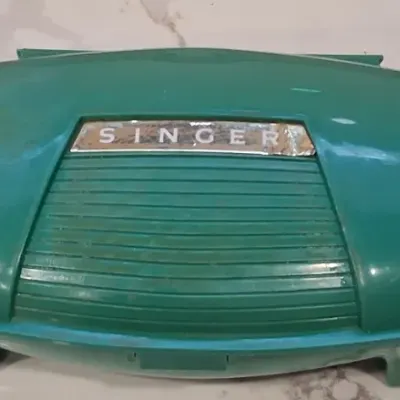 Vintage green plastic Singer sewing machine accessory case, featuring an oval shape and a ribbed center panel with the Singer brand name.