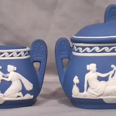 Wedgwood blue jasperware creamer and lidded sugar bowl set, featuring white neoclassical relief figures and wave borders.