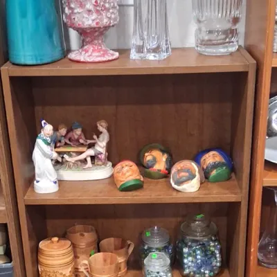 A wooden bookcase filled with collectibles, including a tall turquoise ceramic vase, a textured pink lidded urn, two clear glass vases,...