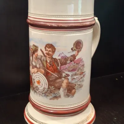 Vintage German-style ceramic beer stein featuring a colorful illustration of a traditional Bavarian couple, complete with an ornate...