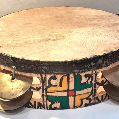 Vintage hand-painted wooden tambourine featuring a natural rawhide drumhead, brass jingles, and colorful geometric folk art designs.
