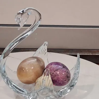 Vintage clear art glass swan bowl holding two polished stone decorative eggs, one in tan alabaster and the other in purple rhodonite.