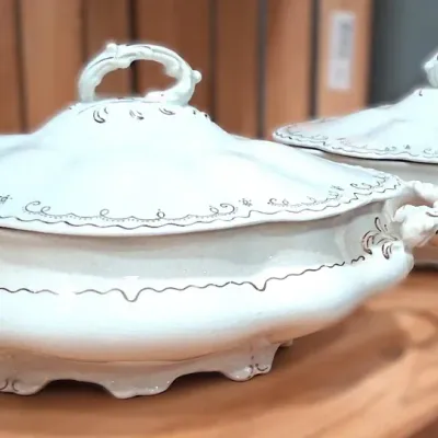 Pair of antique white ironstone covered tureen serving dishes featuring elegant scalloped rims, ornate handles, and delicate gold-painted...