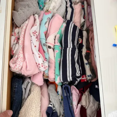 Sale Photo Thumbnail #119: Assorted baby and toddler clothing, including onesies, sweaters, and pants, neatly folded inside a wooden dresser drawer.