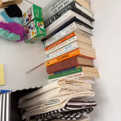 Sale Photo Thumbnail #116: A stack of non-fiction and poetry books alongside Fujifilm Instax Mini film boxes and a collection of fabric drawstring pouches.
