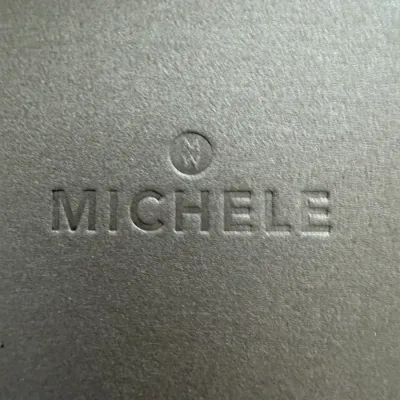 Michele brand logo embossed on a textured grey surface, likely a watch box or packaging.