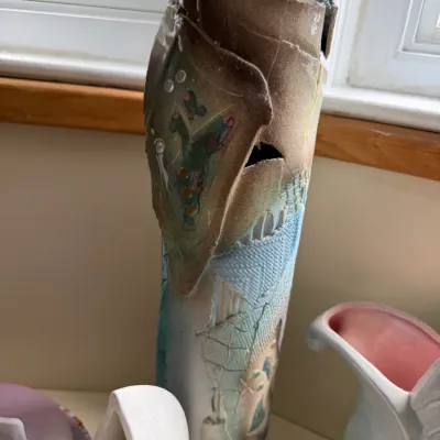 Artisan studio pottery vase featuring a tall, cylindrical form with textured, layered clay elements in earth tones and light blue glazes.