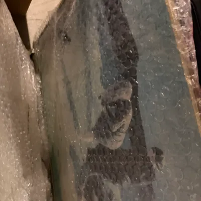 Sale Photo Thumbnail #235: Large framed artwork wrapped in protective bubble wrap, depicting a stylized figure on a light blue background.