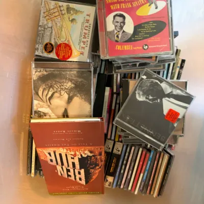 A collection of music CDs and a Ben-Hur soundtrack box set, featuring artists like Frank Sinatra and Tony Bennett, stored in a plastic bin.