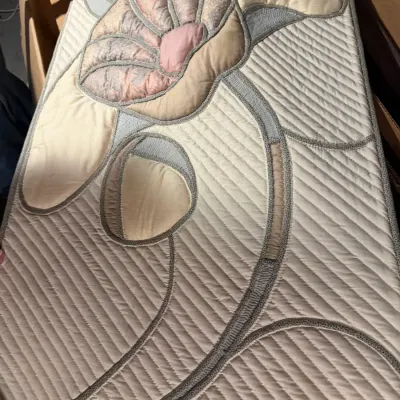Sale Photo Thumbnail #190: Vintage quilted fabric wall hanging or headboard panel featuring a large stylized floral design in pastel pink, cream, and grey tones, circa 1980s.