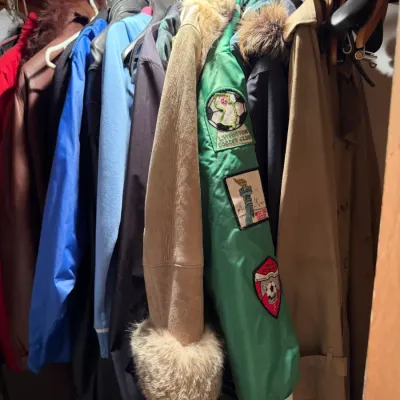 Sale Photo Thumbnail #245: Assorted vintage outerwear hanging in a closet, featuring a green Livingston Soccer Club varsity jacket with patches and a tan suede coat with fur trim.