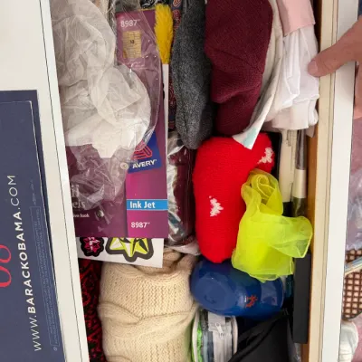 Sale Photo Thumbnail #120: Assorted clothing and accessories inside a drawer, including a cream cable-knit sweater, winter hats, a yellow scarf, and Avery ink jet labels.