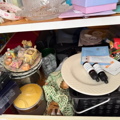 Sale Photo Thumbnail #140: Assorted household items and collectibles, including a small doll in a green crocheted dress, a nesting doll, skincare products, and decorative plates.
