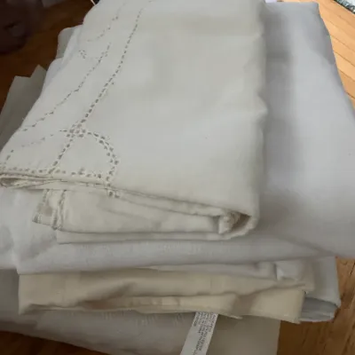 Stack of vintage white and cream linens, including a tablecloth with openwork embroidery details.