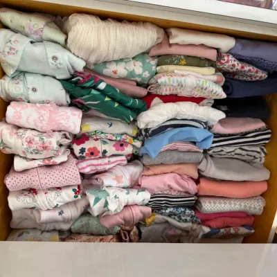 Sale Photo Thumbnail #123: Assortment of folded baby and toddler clothing, featuring various colorful patterns, floral prints, and solid colors, neatly organized inside a wooden drawer.