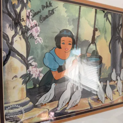 Sale Photo Thumbnail #133: Walt Disney Productions limited edition serigraph of Snow White at the wishing well, signed by Adriana Caselotti, the voice of Snow White, and presented in a matted frame.