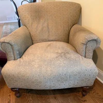 Traditional upholstered armchair featuring a muted green and beige damask pattern, rolled arms, and turned wooden legs.
