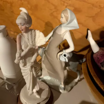 Sale Photo Thumbnail #177: Two vintage porcelain figurines, including a Lladro-style young woman with a donkey and a flapper-style woman with a fan on a wooden base.