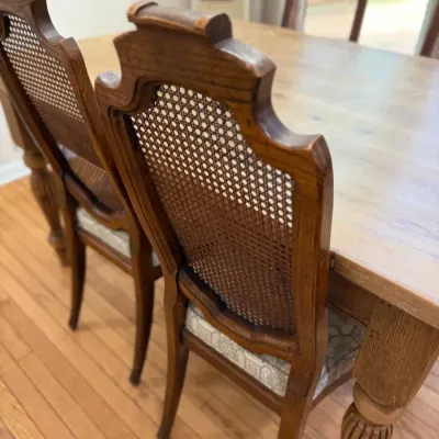 Vintage wooden dining chairs featuring cane backs, upholstered seats, and carved top rails, paired with a matching wooden dining table.