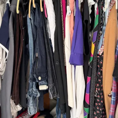 Sale Photo Thumbnail #144: Assorted women's clothing, including jeans, jackets, dresses, and blouses, hanging on a closet rack.