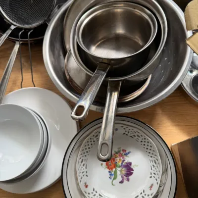 Assorted kitchenware including stainless steel pots, mixing bowls, a mesh strainer, white ceramic bowls, and a decorative floral plate...
