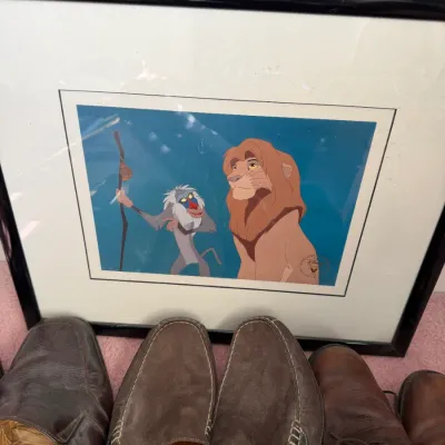 Sale Photo Thumbnail #131: Framed Disney's The Lion King animation cel print featuring Rafiki and Simba, displayed behind several pairs of men's brown leather and suede shoes.
