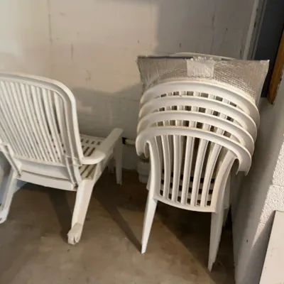Sale Photo Thumbnail #209: White plastic outdoor patio chairs, including a stack of armchairs and a single reclining lounge chair with wheels.