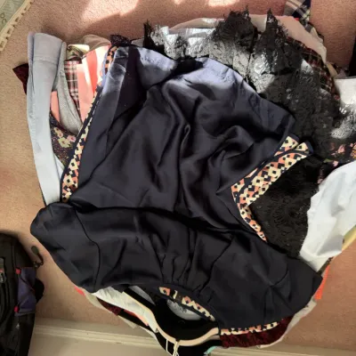 Sale Photo Thumbnail #125: A pile of assorted women's clothing, including a navy blue top with geometric trim and a black lace garment, resting on hangers.