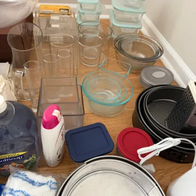 Assorted kitchenware and household items, including glass storage containers with light blue lids, mixing bowls, baking pans, and glassware.
