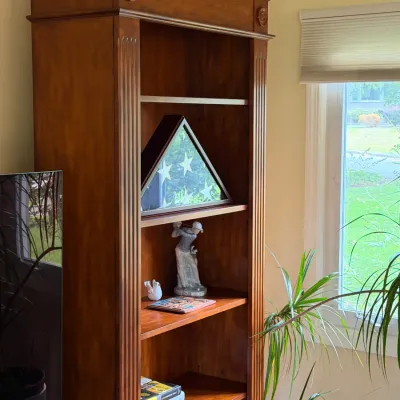 Traditional cherry wood bookcase featuring fluted pilasters, rosette accents, and a crown molding top, displaying a triangular flag case...