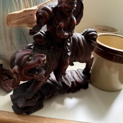 Hand-carved wooden sculpture depicting a Chinese immortal or deity riding a mythical beast, featuring intricate details and a rich dark...