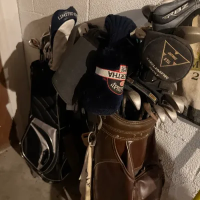 Sale Photo Thumbnail #203: Two golf bags filled with a variety of clubs, including a brown vinyl bag with Callaway Big Bertha and Orlimar headcovers, and a black and silver bag.