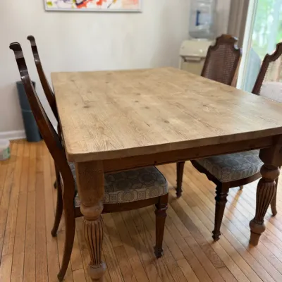 Rustic wooden dining table with turned legs, paired with four upholstered dining chairs featuring cane backs and patterned seat cushions.