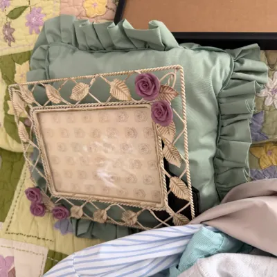 Sale Photo Thumbnail #112: Vintage-style wirework picture frame with gold-painted leaf details and purple rose accents, resting against a ruffled sage green pillow.
