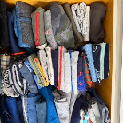 Sale Photo Thumbnail #124: Assorted children's clothing, including shirts, pants, and hoodies, neatly folded and organized inside a wooden dresser drawer.