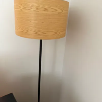 Modern floor lamp featuring a slender black metal pole and a drum shade with a light wood grain finish.