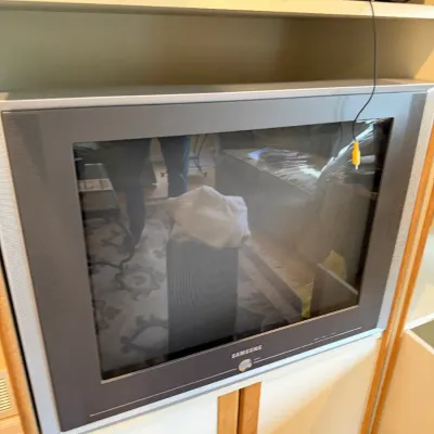 Vintage Samsung CRT television with a silver and grey bezel, housed in a wooden entertainment center with a DVD player on the shelf above.