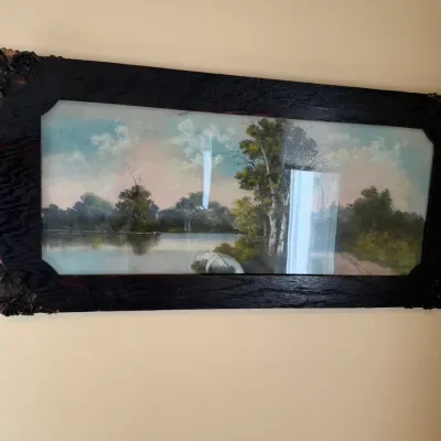Antique panoramic landscape print depicting a serene river scene, housed in a wide, dark-stained oak frame with ornate corner details,...