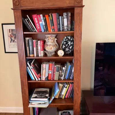 Neoclassical style cherry wood bookcase featuring fluted pilasters, rosette details, and a prominent crown molding, filled with books and...