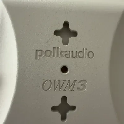 Close-up of the back of a white Polk Audio OWM3 multi-purpose home theater speaker, showing the keyhole slots for wall mounting.