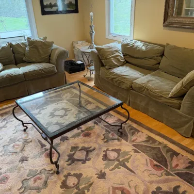 Living room set featuring a matching olive green sofa and loveseat with slipcovers, paired with a glass-top coffee table on a wrought...