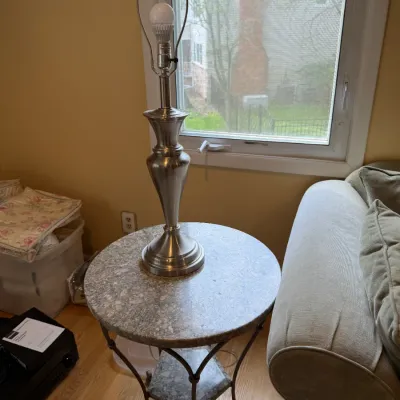 Contemporary round side table with a faux-stone top and metal legs, paired with a brushed nickel table lamp.