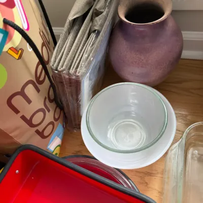 Assorted household items including a purple ceramic vase, glass mixing bowls, a red baking dish, and packaged fabric organizers.