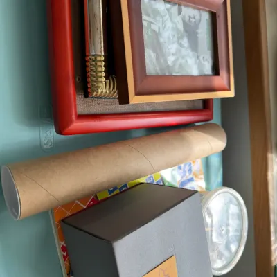 Assorted household items including a red picture frame, a cardboard mailing tube, and a small grey box with a sticky note.