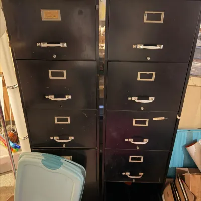 Sale Photo Thumbnail #214: Two vintage black metal four-drawer filing cabinets with silver-toned handles and label holders, showing some wear from use.