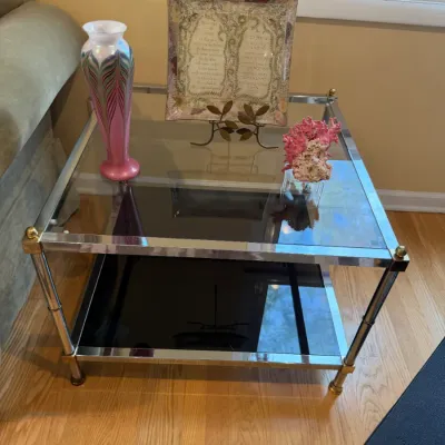 Mid-century modern chrome and brass two-tier end table with a clear glass top shelf and a smoked glass bottom shelf, displaying...