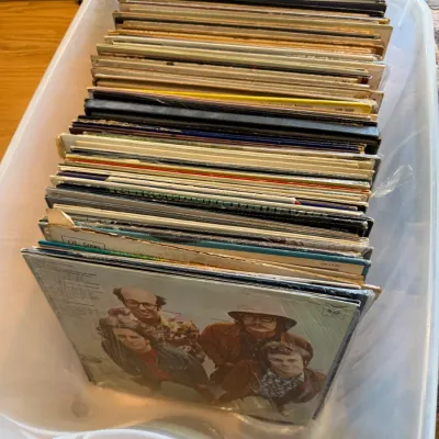 Large collection of vintage vinyl LP records stored in a clear plastic storage bin, showing various wear on the sleeves.