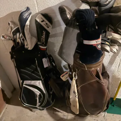 Sale Photo Thumbnail #204: Two golf bags filled with clubs, including a modern black and silver stand bag with Titleist headcovers and a vintage brown vinyl cart bag.